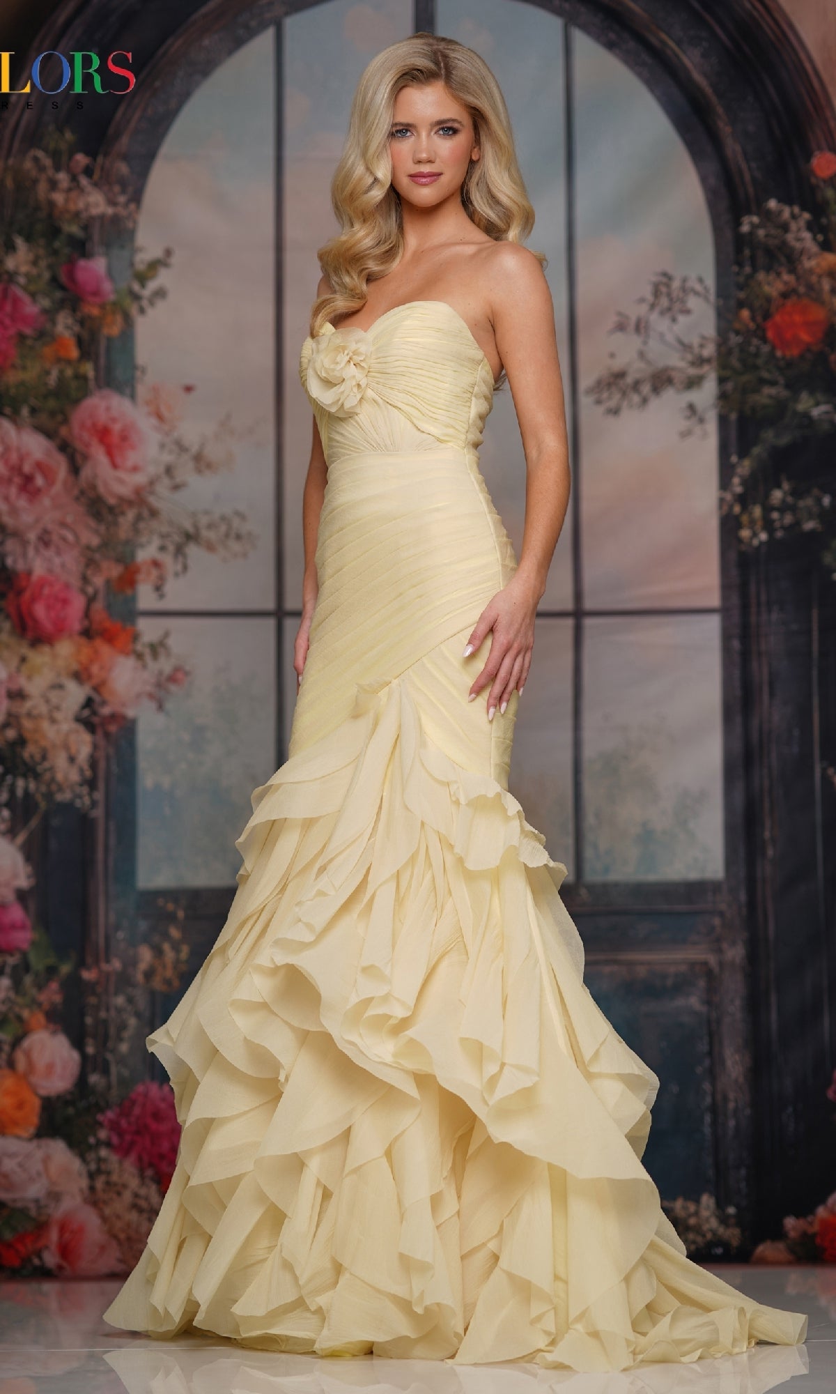 A woman in a yellow Strapless Chiffon Prom Gown (Colors Dress 3886) poses before a floral and arched window backdrop.